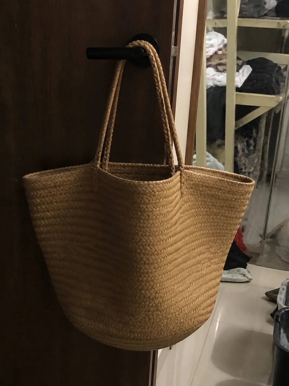 Original: straw tote bag hanging on a door handle in dim light